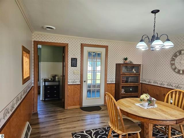 dining space with dark wood-type flooring, crown molding, a notable chandelier, and wood walls