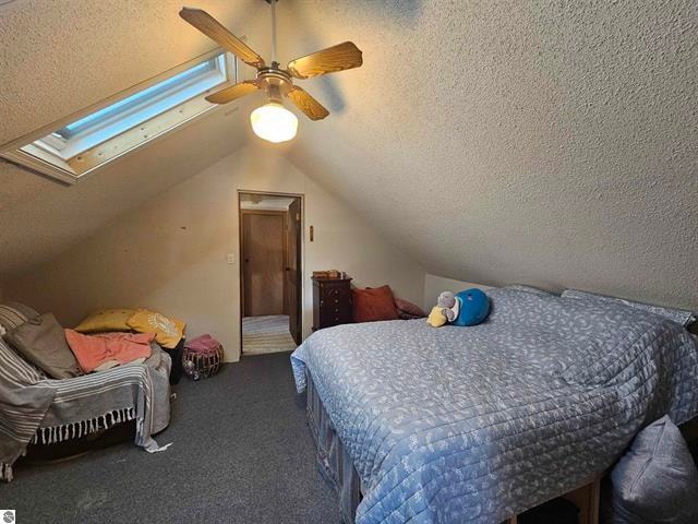 bedroom featuring dark colored carpet, lofted ceiling with skylight, a textured ceiling, and ceiling fan