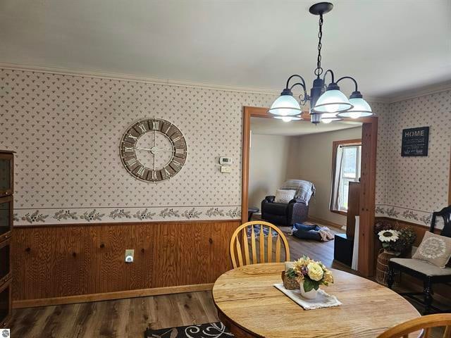 dining area featuring an inviting chandelier, wooden walls, wood-type flooring, and crown molding