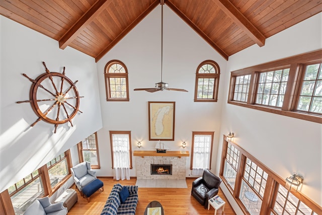 living room featuring a stone fireplace, ceiling fan, light hardwood / wood-style floors, wooden ceiling, and high vaulted ceiling