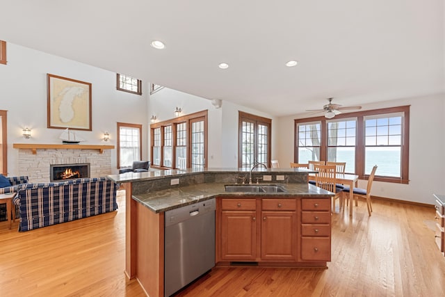 kitchen featuring stainless steel dishwasher, light wood-type flooring, a fireplace, sink, and a water view