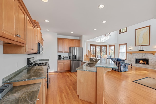 kitchen featuring appliances with stainless steel finishes, sink, a stone fireplace, light hardwood / wood-style floors, and a breakfast bar area