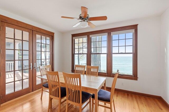 dining space with french doors, ceiling fan, a water view, and light wood-type flooring