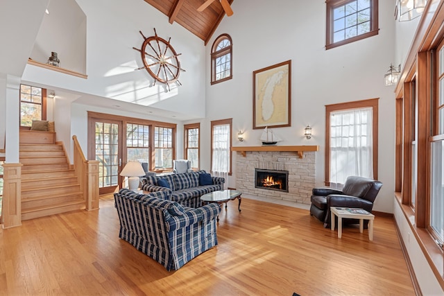 living room featuring high vaulted ceiling, wood ceiling, a stone fireplace, beam ceiling, and hardwood / wood-style flooring