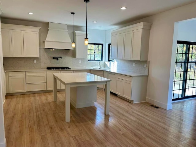 kitchen featuring decorative backsplash, hanging light fixtures, black gas cooktop, custom exhaust hood, and light hardwood / wood-style floors