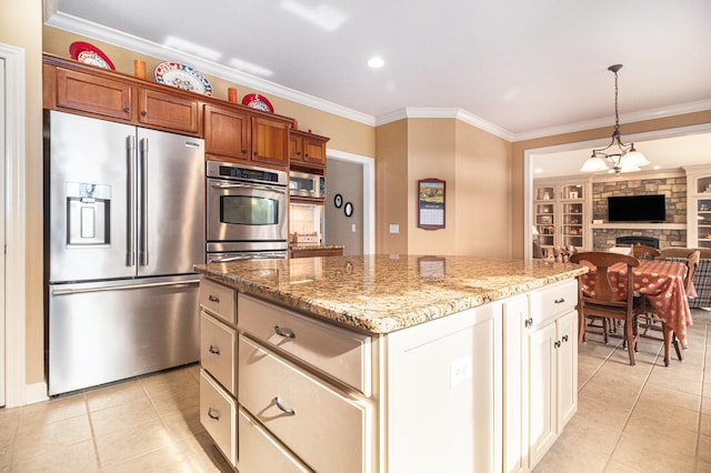 kitchen with a kitchen island, appliances with stainless steel finishes, ornamental molding, pendant lighting, and a stone fireplace