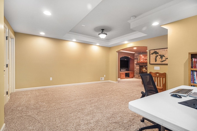 carpeted office space with a stone fireplace and a raised ceiling