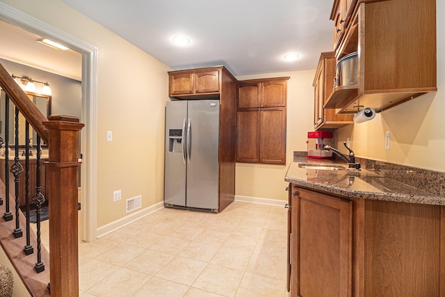 kitchen featuring stainless steel refrigerator with ice dispenser, dark stone countertops, and sink