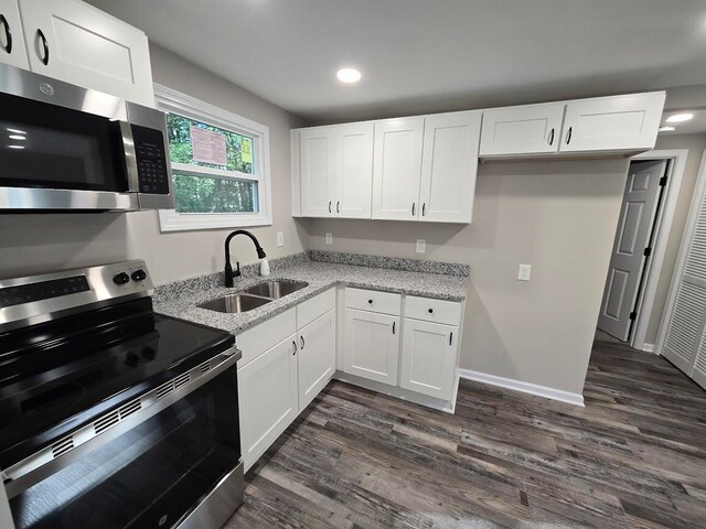 kitchen with dark wood-type flooring, stainless steel appliances, sink, white cabinets, and light stone counters