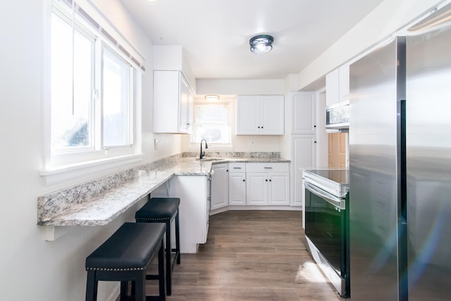 kitchen with stainless steel appliances, wood-type flooring, sink, a breakfast bar, and white cabinets