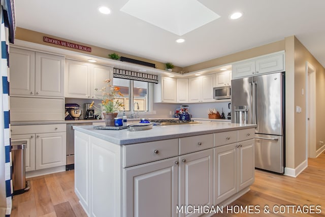 kitchen with appliances with stainless steel finishes, white cabinetry, light wood-type flooring, a skylight, and a center island