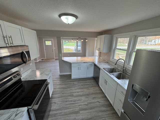 kitchen featuring appliances with stainless steel finishes, sink, kitchen peninsula, hardwood / wood-style floors, and white cabinetry