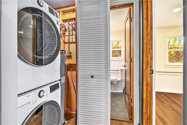 laundry area with stacked washer / dryer, a healthy amount of sunlight, wood-type flooring, and ornamental molding