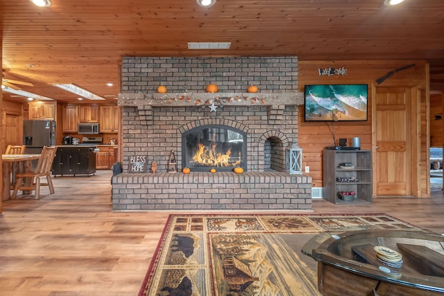 living room with a fireplace, wooden ceiling, light wood-type flooring, and a skylight