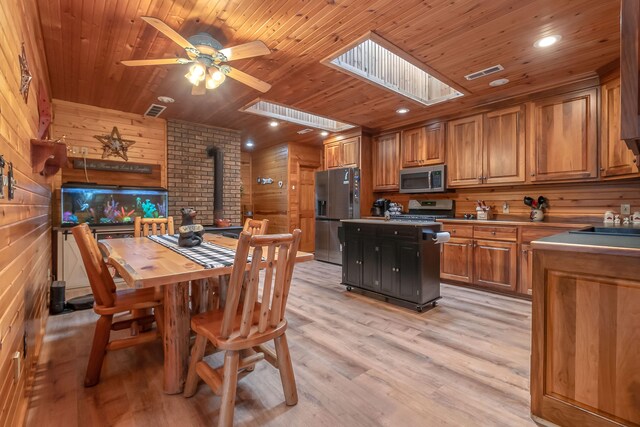 dining area featuring a skylight, wooden walls, light hardwood / wood-style floors, and a wood stove