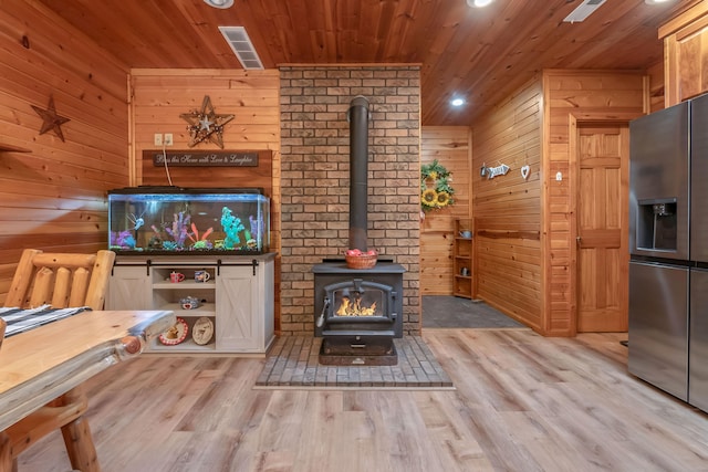 living room with wood walls, light hardwood / wood-style floors, wooden ceiling, and a wood stove