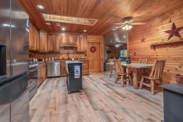 kitchen featuring light hardwood / wood-style flooring, wood walls, ceiling fan, a skylight, and appliances with stainless steel finishes