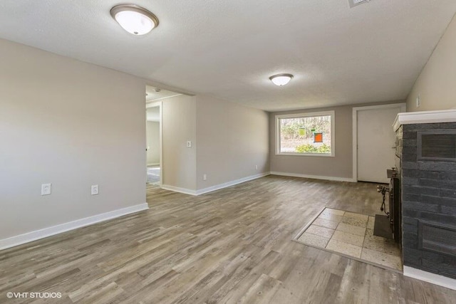 unfurnished living room with a fireplace, light hardwood / wood-style floors, and a textured ceiling