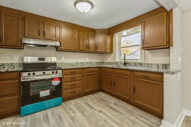 kitchen featuring light stone countertops, stainless steel stove, sink, and light hardwood / wood-style floors