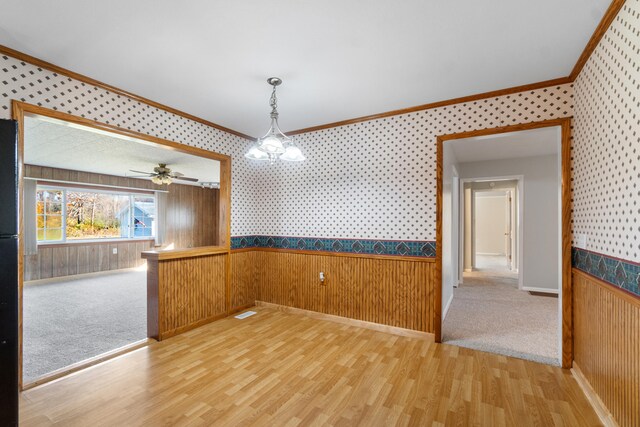 unfurnished dining area featuring ornamental molding, hardwood / wood-style flooring, wooden walls, and ceiling fan with notable chandelier