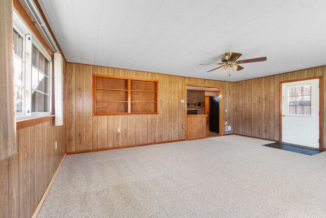 empty room with light carpet, built in features, wooden walls, and ceiling fan