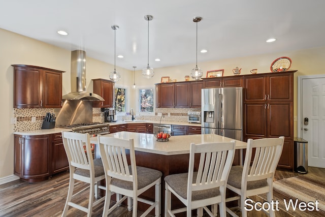 kitchen with sink, appliances with stainless steel finishes, a kitchen island, decorative light fixtures, and wall chimney exhaust hood