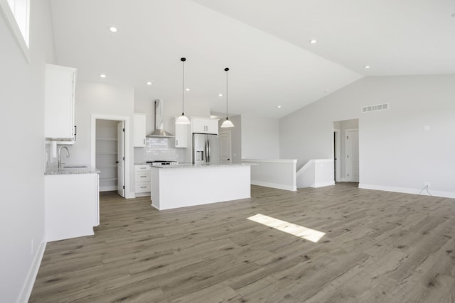 kitchen featuring wall chimney range hood, white cabinets, hanging light fixtures, a kitchen island, and stainless steel refrigerator with ice dispenser