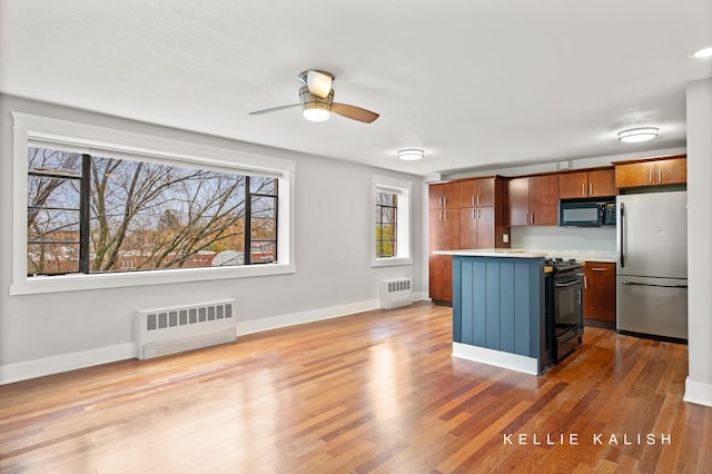 kitchen featuring light hardwood / wood-style floors, radiator heating unit, black appliances, and a kitchen island