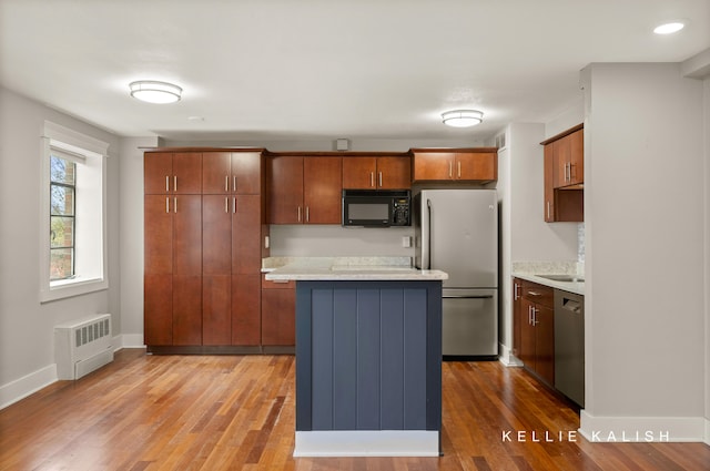 kitchen with stainless steel appliances, wood-type flooring, radiator heating unit, and a kitchen island