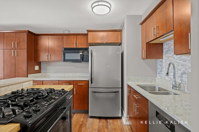 kitchen featuring light hardwood / wood-style floors, sink, black appliances, light stone counters, and decorative backsplash