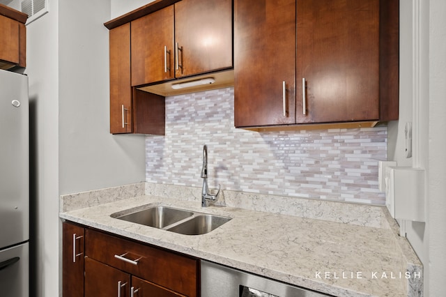 kitchen with backsplash, light stone counters, sink, and stainless steel refrigerator