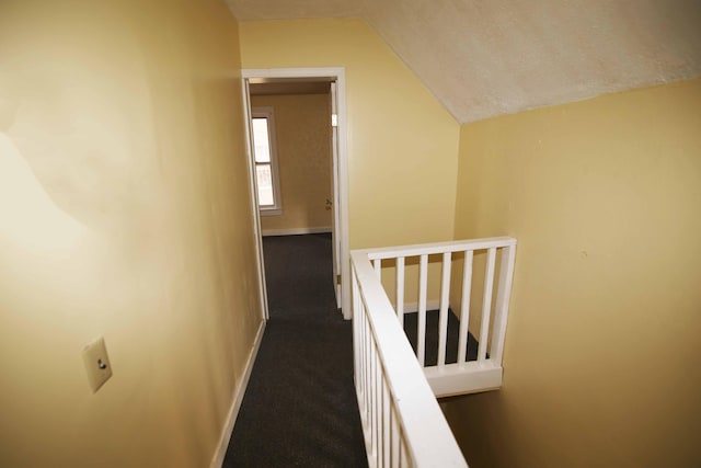 corridor with a textured ceiling, dark carpet, and vaulted ceiling