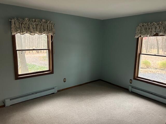 carpeted spare room featuring baseboard heating and plenty of natural light