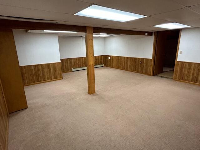 basement featuring light carpet, a paneled ceiling, and wooden walls