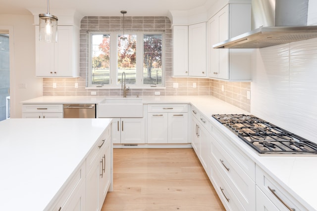 kitchen featuring hanging light fixtures, wall chimney exhaust hood, sink, and appliances with stainless steel finishes