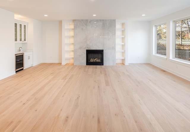 unfurnished living room featuring wine cooler, light wood-type flooring, wet bar, and a premium fireplace