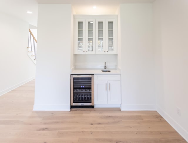 bar featuring light hardwood / wood-style flooring, beverage cooler, sink, and white cabinets