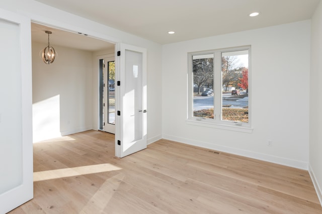 unfurnished room featuring an inviting chandelier and light hardwood / wood-style flooring