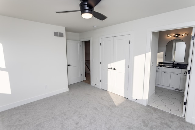 unfurnished bedroom featuring sink, ceiling fan, light colored carpet, connected bathroom, and a closet