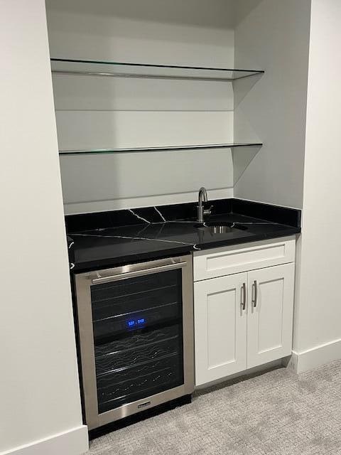 bar with white cabinetry, light carpet, beverage cooler, and sink