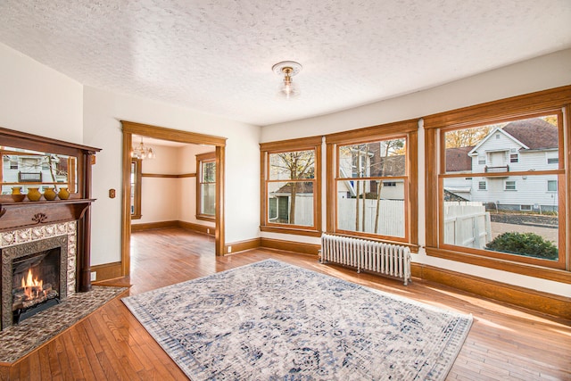 interior space featuring a textured ceiling, radiator heating unit, light hardwood / wood-style floors, a notable chandelier, and a premium fireplace