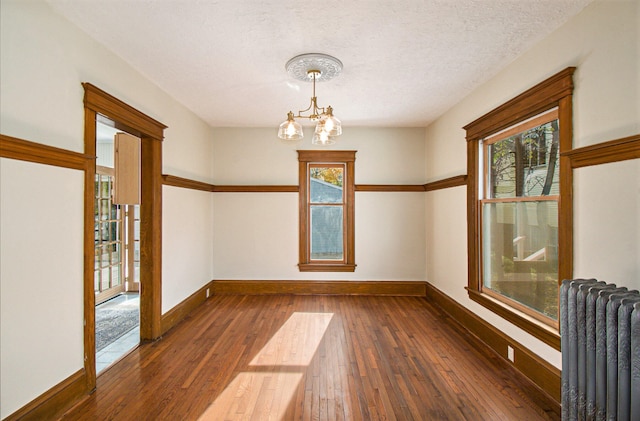 empty room with dark hardwood / wood-style flooring, a chandelier, a textured ceiling, and radiator