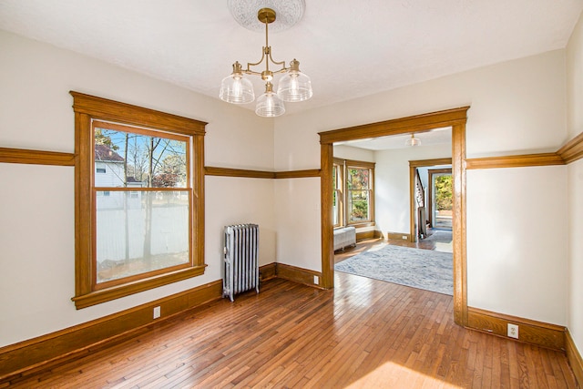 unfurnished room with radiator, hardwood / wood-style flooring, a wealth of natural light, and a chandelier