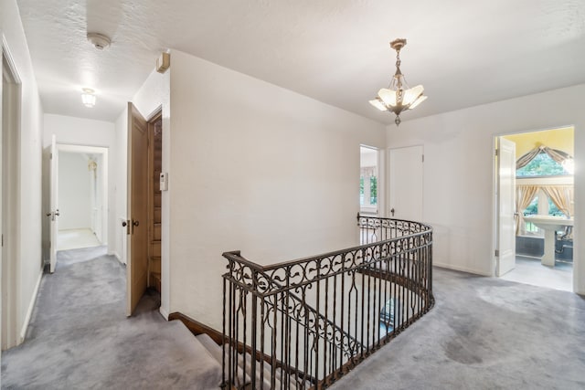 hall featuring a textured ceiling, carpet floors, and an inviting chandelier