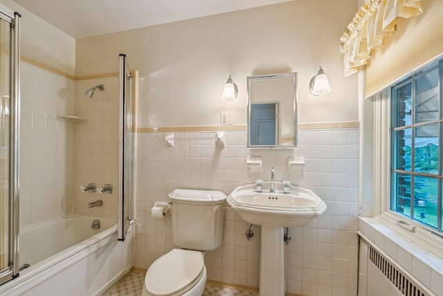 full bathroom with toilet, radiator heating unit, bath / shower combo with glass door, and tile walls