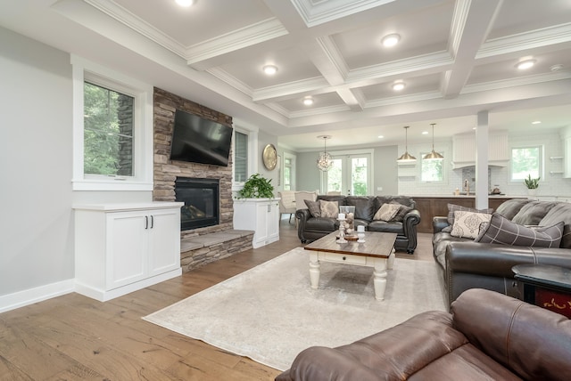 living room with coffered ceiling, light hardwood / wood-style floors, a stone fireplace, and crown molding