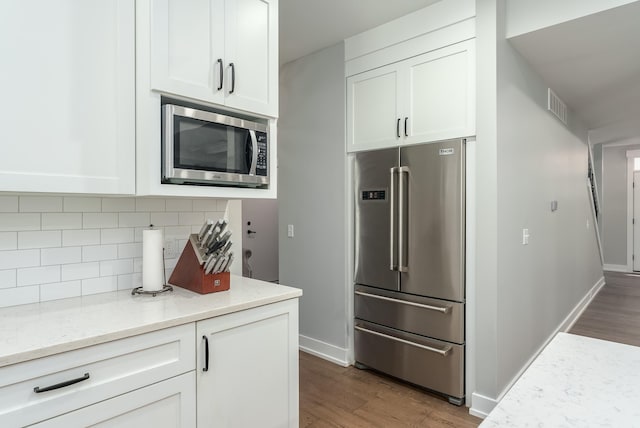 kitchen featuring backsplash, white cabinetry, appliances with stainless steel finishes, light stone counters, and light hardwood / wood-style floors