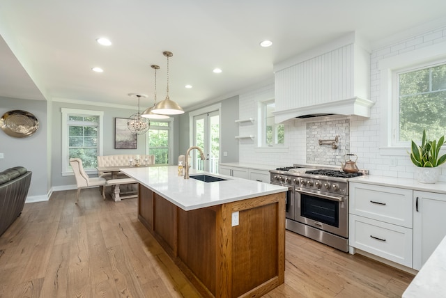 kitchen featuring white cabinets, high end stainless steel range oven, light wood-type flooring, decorative light fixtures, and sink