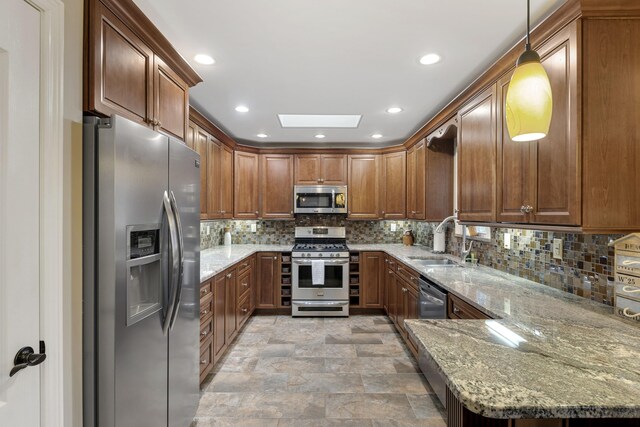 kitchen featuring a skylight, sink, light stone counters, pendant lighting, and appliances with stainless steel finishes