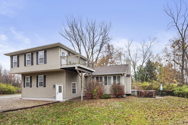 view of side of property with a balcony, a hot tub, and a lawn